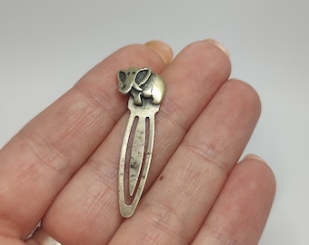 May include: A silver-toned metal bookmark with an elephant design. The elephant is sitting on its hind legs with its trunk raised.