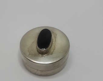 May include: A small, round, silver trinket box with a black oval stone on the lid.