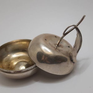 Puede incluir: Azucarero de plata con forma de manzana con tapa con bisagras y asa decorativa. El cuenco está abierto y la tapa está quitada.