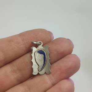 May include: Silver pendant with a blue and white image of the Virgin Mary. The pendant is in the shape of a rectangle with a scalloped edge.