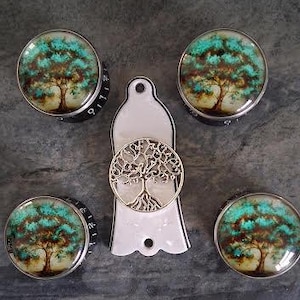 May include: A selection of cabinet knobs and a key holder. The knobs display a tree design with teal and brown hues. The key holder features a tree of life design. The knobs have a black base with white numbers.