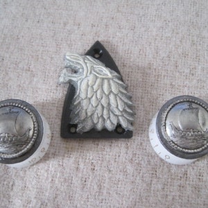 Puede incluir: Tres pomos de guitarra plateados con una cabeza de lobo y un diseño de barco. La cabeza de lobo está sobre una base de plástico negro.