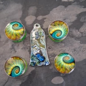 May include: An assortment of decorative items featuring a spiral design in shades of teal, yellow, and green. The collection includes three round pieces and a long, irregular-shaped pendant, all with a metallic border.