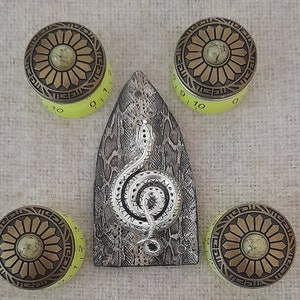 Könnte beinhalten: Vier gelbe und goldene Knöpfe mit einem Blumendesign und einem silbernen Violinschlüssel mit einem Schlangendesign auf grauem Hintergrund.