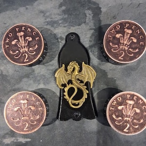 May include: A black key fob featuring a gold dragon design, accompanied by four bronze two pence coins. The coins display the text "TWO PENCE" and the number "2".