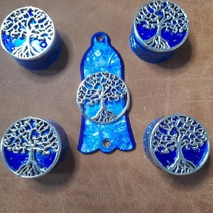 May include: Five blue and silver tree of life plugs and a matching pendant. The plugs are cylindrical with a silver tree design on top. The pendant is a blue teardrop shape with a silver tree of life design.