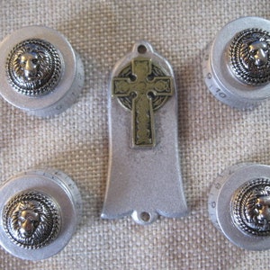 Puede incluir: Cinco pomos plateados con diseños de cabeza de león y un colgante de cruz plateada. Los pomos tienen los números 9, 10, 11, 12 y 15.