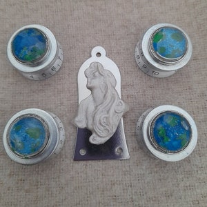 May include: Five silver guitar knobs with a blue and green globe design. The knobs have numbers 1-10 and 1-7. A silver guitar pickguard with a white sculpted female bust.