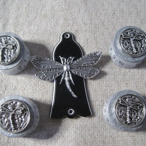 Puede incluir: Cinco pomos de guitarra plateados con un diseño de libélula. Cada pomo tiene un fondo negro con una libélula plateada y los números 9, 10, 11, 12 y 1 impresos en el pomo.