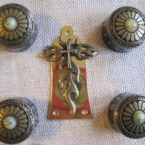 May include: Set of five gold-tone metal guitar knobs with a floral design and a cross in the centre. The knobs are for a guitar and have a decorative look.