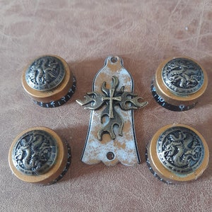 May include: Five gold-colored metal knobs with black accents and a decorative design. The knobs feature a cross and a dragon-like creature. The knobs are arranged in a semi-circle around a white and gold decorative piece.