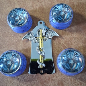 May include: An assortment of fantasy-themed items. Includes four purple-rimmed dials with a dragon image and a silver pendant with a dragon-wrapped sword design. The background is a brown leather-like surface.
