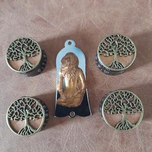May include: Four round metal knobs with a tree of life design and a metal pendant with a woman figure. The knobs are gold and black with a copper-colored tree of life design. The pendant is black with a gold woman figure.