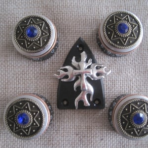 Könnte beinhalten: Satz von fünf Gitarrenknöpfen mit einem silbernen Kreuz- und Flammen-Design. Die Knöpfe sind rund und haben eine silberne und goldene Oberfläche mit blauen Edelsteinen in der Mitte.