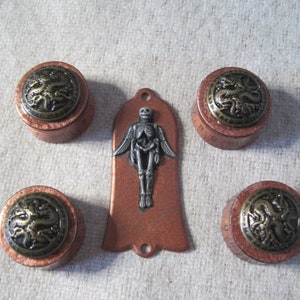 May include: A collection of copper-toned decorative items. Four round pieces with a dragon design on top and a bell-shaped pendant with a skeleton figure. The items have a vintage, gothic aesthetic.
