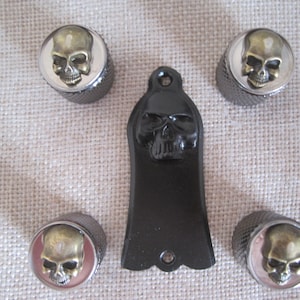May include: Set of five guitar knobs with skull designs. The knobs are silver with a gold skull design. The knobs are for a guitar and are a decorative addition to the instrument.