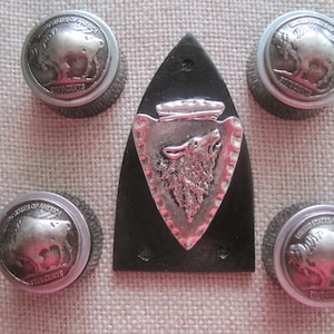 Könnte beinhalten: Fünf silberfarbene US-Nickel mit einem Büffeldesign sind um einen schwarzen Lederfleck mit einem silberfarbenen Wolfskopfdesign angeordnet. Die Nickelmünzen tragen die Inschriften "United States of America" und "Five Cents".