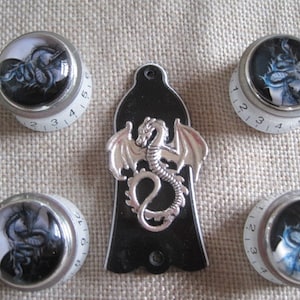 Könnte beinhalten: Satz von sechs silbernen Gitarrenknöpfen mit schwarzen und weißen Drachenmotiven. Die Knöpfe sind mit den Zahlen 1-5 und 1-4 bedruckt. Die Knöpfe sind für eine Gitarre.