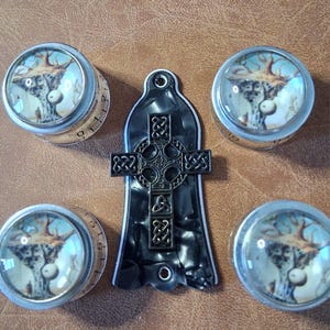 Könnte beinhalten: Eine Sammlung von Gitarrenteilen, darunter fünf silberne Knöpfe mit einer Baumszene unter einer Glaskuppel und ein schwarzes Schlagbrett mit keltischem Kreuzdesign. Die Knöpfe haben weiße Zahlenmarkierungen.