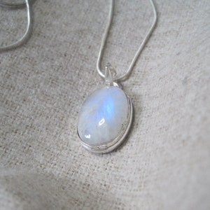 May include: A silver chain necklace with a moonstone pendant. The moonstone is oval shaped and has a milky white colour with a blue iridescent sheen.