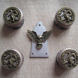 Puede incluir: Conjunto de cinco botones de guitarra dorados con un diseño de dragón y una placa de protección de guitarra plateada con un diseño de calavera y alas.