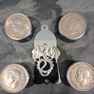 May include: A silver dragon pendant with a black backing, displayed with four vintage coins. The coins show a profile of a man and text around the edge. The pendant has a loop at the top for hanging.