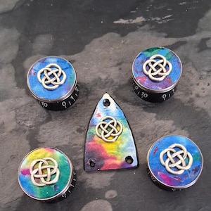 May include: Five decorative knobs and a triangular piece with a Celtic knot design. The knobs feature a silver knot on a vibrant background of blue, purple, and green. The triangular piece has a similar design and colour scheme.