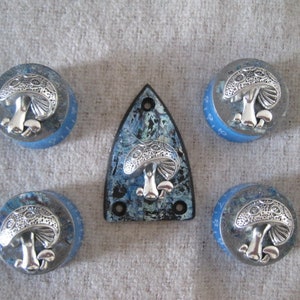 Pode incluir: Cinco botões em forma de cogumelo azuis e prateados com um protetor de guitarra azul e prateado no centro.