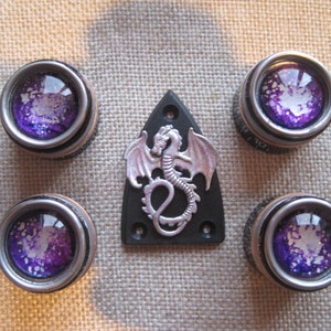 May include: Five silver guitar knobs with purple and white galaxy-like designs. A silver dragon is on a black guitar pickguard.
