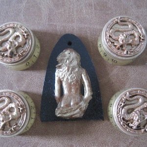 Puede incluir: Cinco pomos de color dorado con un diseño de dragón y números del 0 al 12. Los pomos están sobre una superficie marrón.