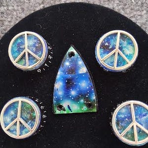 May include: A selection of peace sign and galaxy-themed jewellery. The set includes four round peace sign pendants with a silver border and a triangular pendant. The pendants feature a blue, green, and white galaxy design.