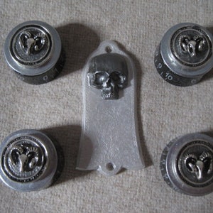 Puede incluir: Seis botones de guitarra plateados con un diseño de calavera negra y cabeza de carnero. Los botones tienen los números 9, 10, 7, 8 y 0 impresos.