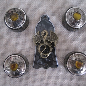 May include: Set of four black and silver guitar knobs with a yellow centre and a black and white guitar pickguard with a gold dragon design.