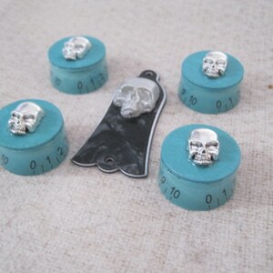 Puede incluir: Cinco pomos turquesa con detalles de calavera plateada. Cada pomo tiene un dial circular con los n&uacute;meros del 0 al 12.