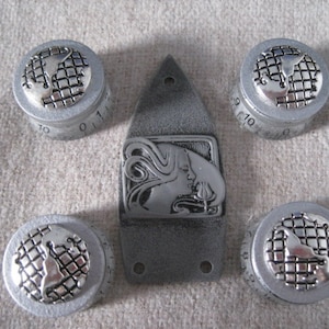 May include: Five silver knobs with a globe design and numbers 0-10. The knobs are on a grey background. The knobs are for a guitar or other musical instrument.