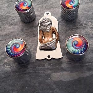 May include: Four silver thimbles with a textured surface and a glass-like top with a swirling spiral design in red, orange, yellow, blue, and green. A pendant with a sculpted figure is also present. The items are arranged on a dark grey surface.