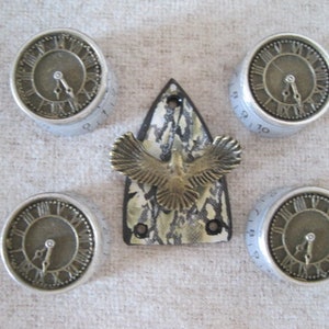 May include: Five silver clock knobs with Roman numeral faces and black hands. The knobs are arranged in a circle around a silver and black decorative piece with a bird design.