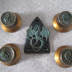Peut inclure: Cinq boutons dorés avec un motif de crâne et le texte "Gretsch" et "69" dessus. Un pickguard de guitare en plastique noir avec un motif de dragon en métal vert.