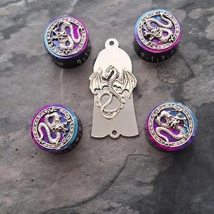Puede incluir: Un conjunto de piezas de guitarra, que incluye cuatro perillas negras y moradas con un diseño de dragón y un golpeador plateado con forma de dragón. Las perillas tienen un degradado de azul, morado y rosa. Los artículos están dispuestos sobre una superficie gris.