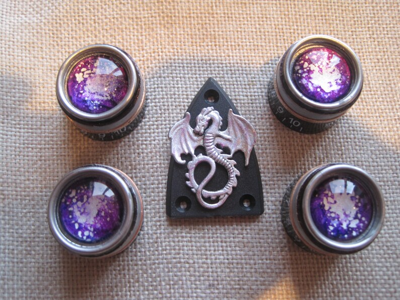 May include: Set of five silver guitar tuning knobs with purple and white galaxy-themed designs. The knobs are surrounded by a silver trim. A silver dragon pickguard is also included.