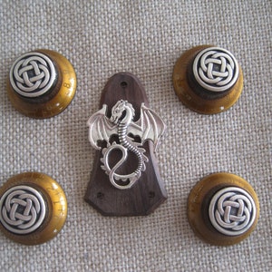 Puede incluir: Cinco pomos dorados con diseños de nudos celtas plateados y una placa de protección de guitarra de madera con un diseño de dragón plateado.