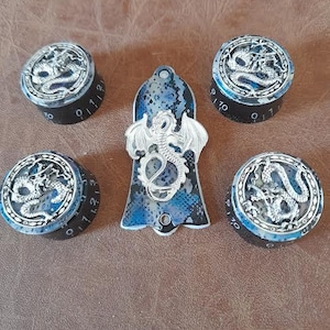May include: Four black and blue guitar knobs with silver dragon designs and a black and blue guitar pickguard with a silver dragon design.