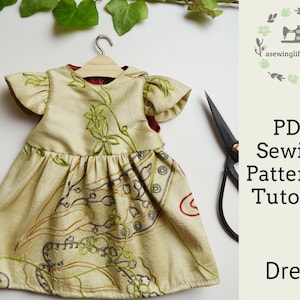 May include: A beige dress with green embroidery and a red lining. The dress is hanging on a wooden hanger. The image includes the text "PDF Sewing Pattern & Tutorial Dress" and a website address.