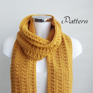 May include: A mustard yellow crocheted scarf with fringe on the ends. The scarf is displayed on a white mannequin. The text "Pattern" is written in black on a white background above the scarf.