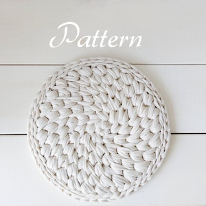 May include: A white crocheted round coaster with a woven pattern. The coaster is on a white wooden surface. The word "Pattern" is written in white above the coaster.