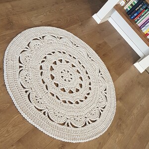 May include: A white crocheted round rug with a lacy design. The rug is on a wooden floor.