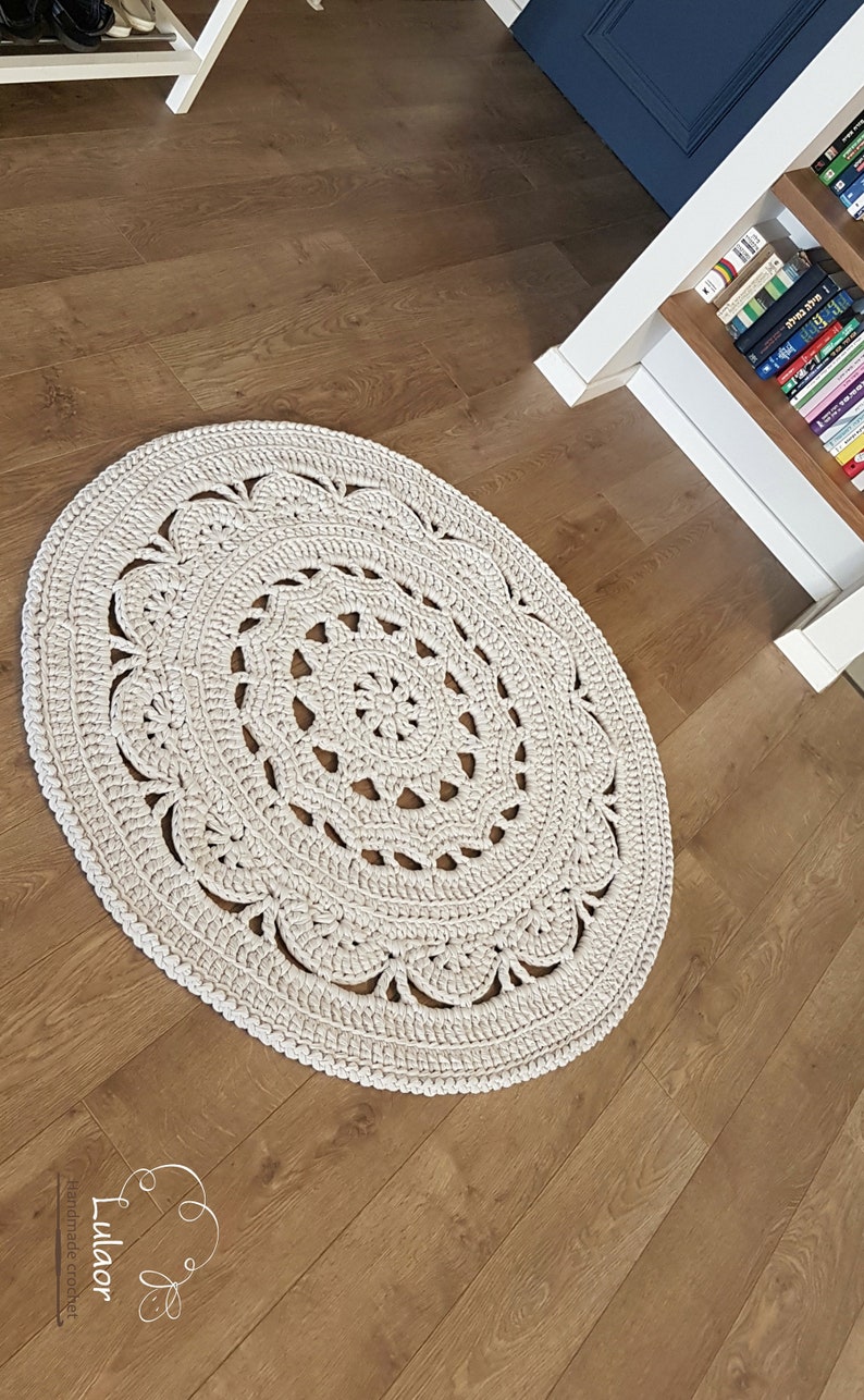 May include: A white crocheted round rug with a lacy design. The rug is on a wooden floor.