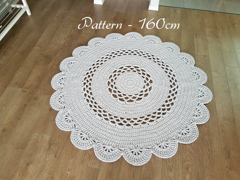 May include: A round, light gray crocheted rug with a scalloped edge. The rug is approximately 63 inches in diameter and features a detailed openwork design in the center. The rug is handmade and placed on a wooden floor.