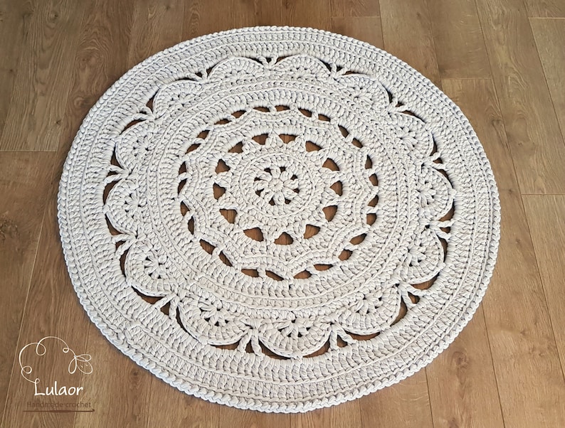 May include: A white crocheted round rug with a delicate lace pattern. The rug has a circular design with a central motif and a border of intricate crocheted details.