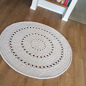 May include: A white crocheted round rug with a circular pattern. The rug is on a wooden floor.